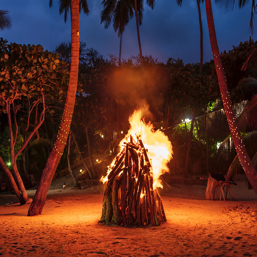 A bonfire burning on the sand at night at Playa Grande, ringed by palm trees strung with lights